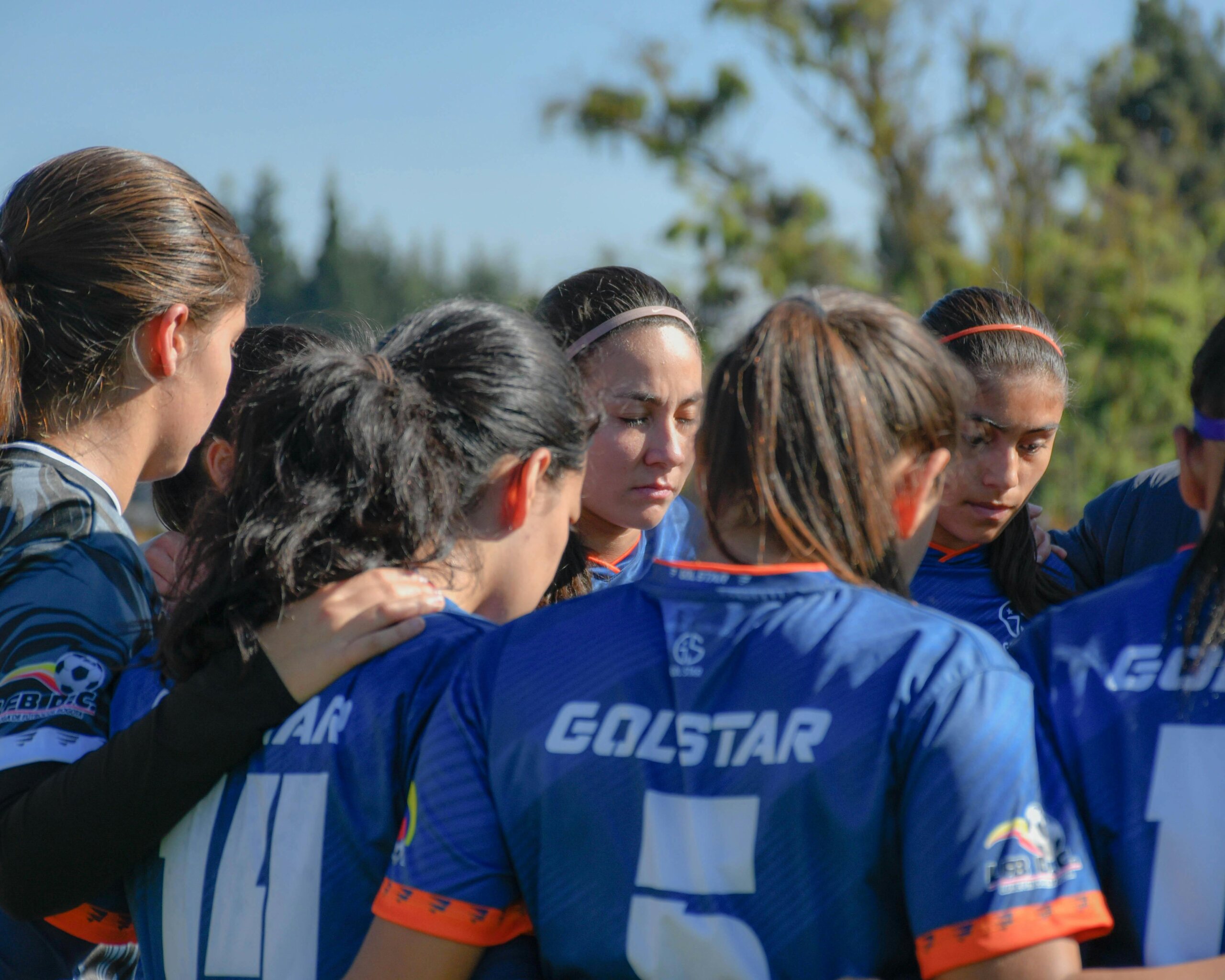 Female soccer players in team huddle with sponsor name on jersey